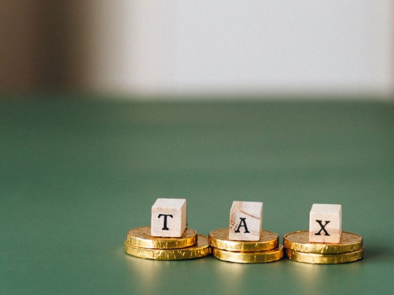 Three stacks of coins, each with a block that spells out "TAX." This image is intended for the blog post titled, "Tax Compliance Tips for Small Businesses."