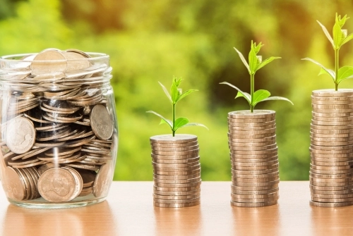 A jar of coins beside two stacks of coins with sporuts growing out of them to signify growing your investment or income. This photo is intended for the blog post, "What is Taxable Income?" written by the Raleigh CPAs at C.E. Thorn, CPA, PLLC.